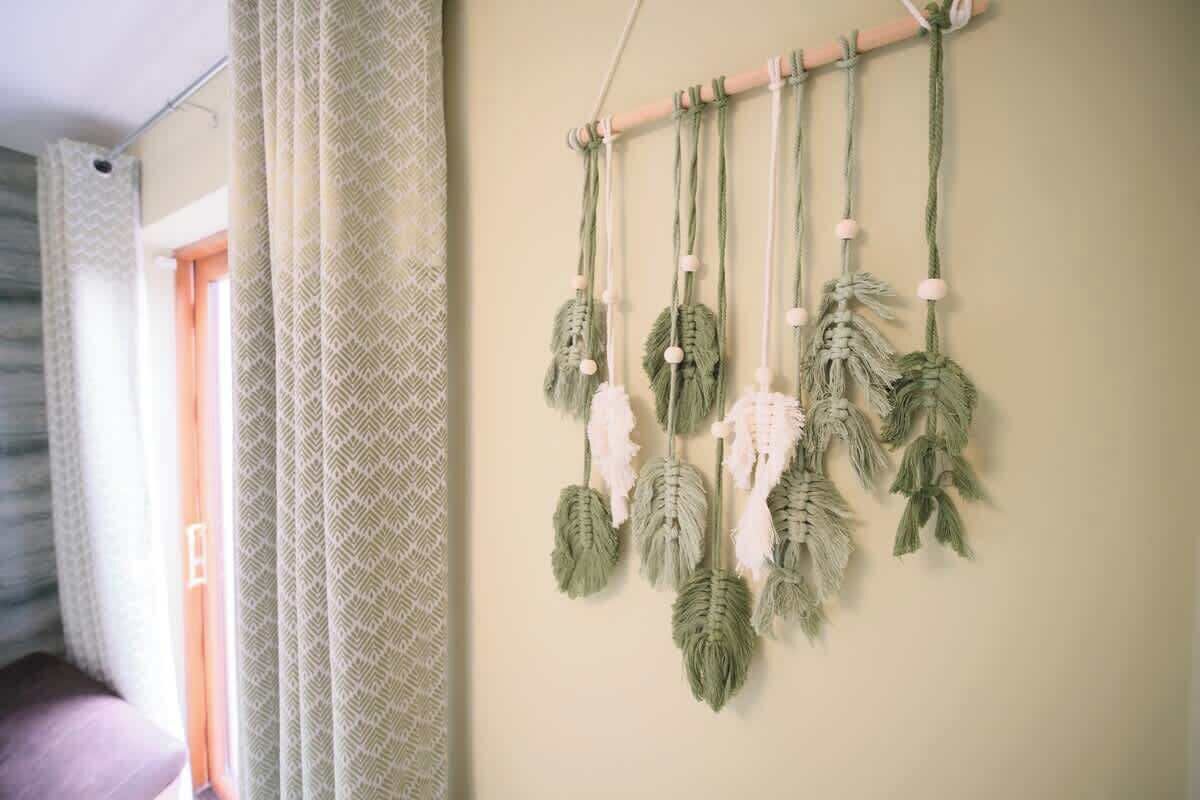 Une décoration murale en macramé avec une tige de suspension, un rideau à motifs et une fenêtre donnant sur un paysage.