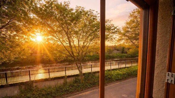 Una vista attraverso una finestra: un fiume, un ponte, alberi e un tramonto.