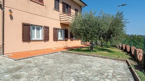 A two-story building with a stone-paved entrance and a small garden area with trees and a fence. - Casa Teresa with Mountain View, Private Terrace, and Wi-Fi (Loppeglia)