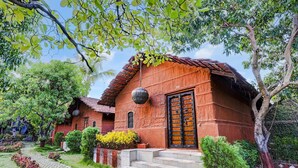 A rustic building with a tiled roof, a wooden door, and a stone pathway leading to the entrance. - Palette Palghar Irayos Resort (Dahanu)