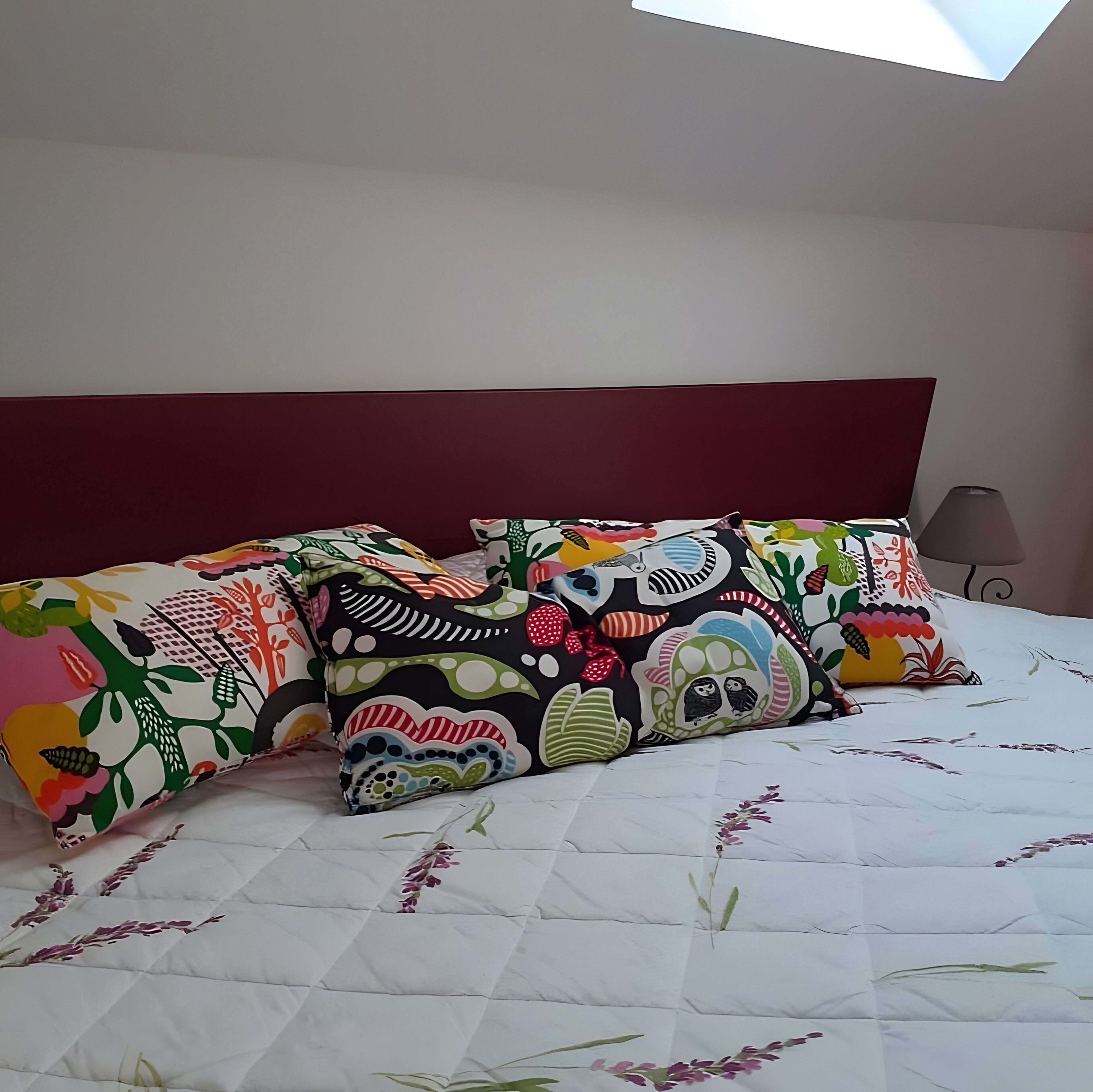 A bed with a floral quilt, a red headboard, and colorful pillows.