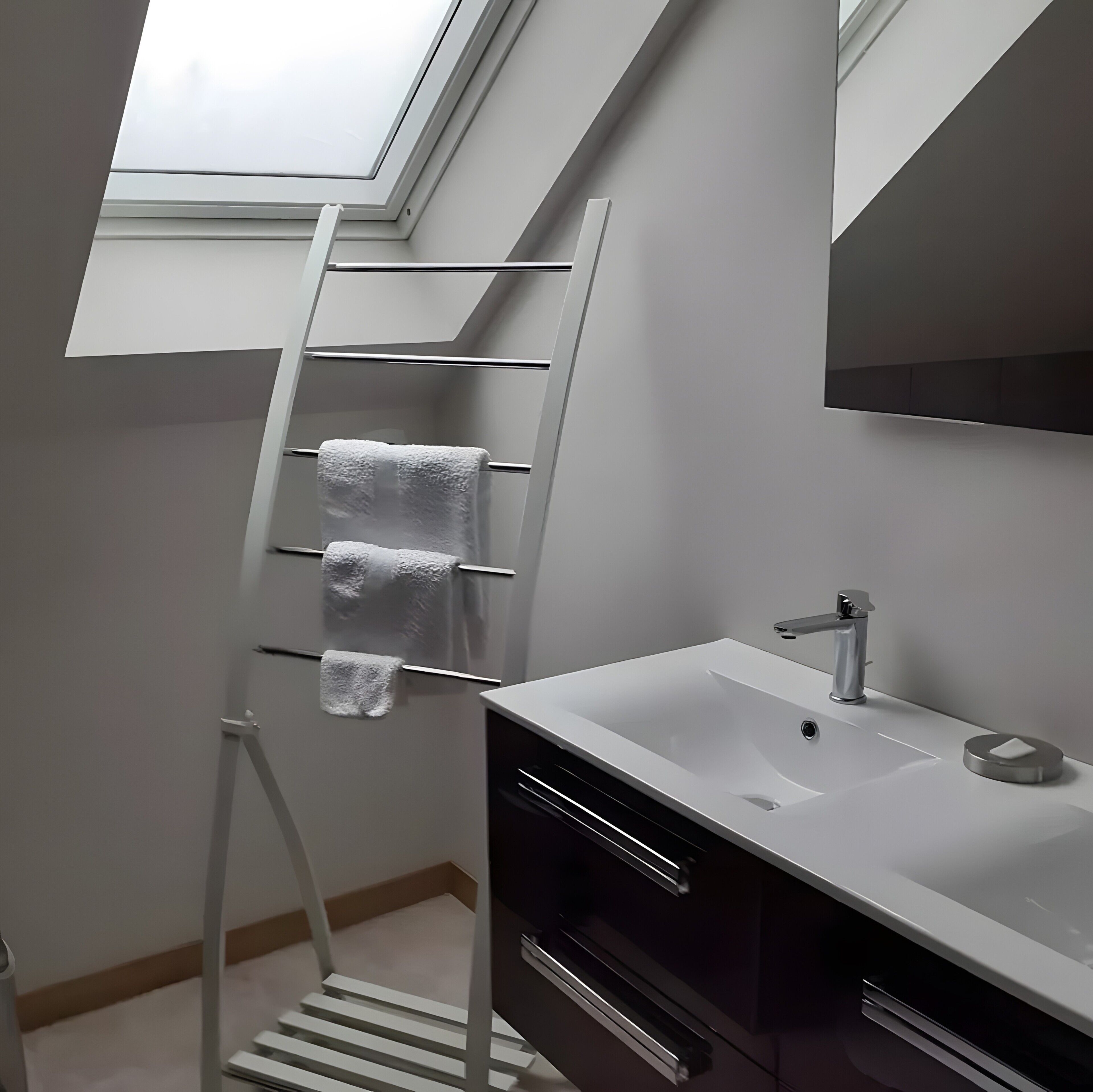 Une salle de bain moderne avec un puits de lumière, un lavabo blanc et un porte-serviettes.