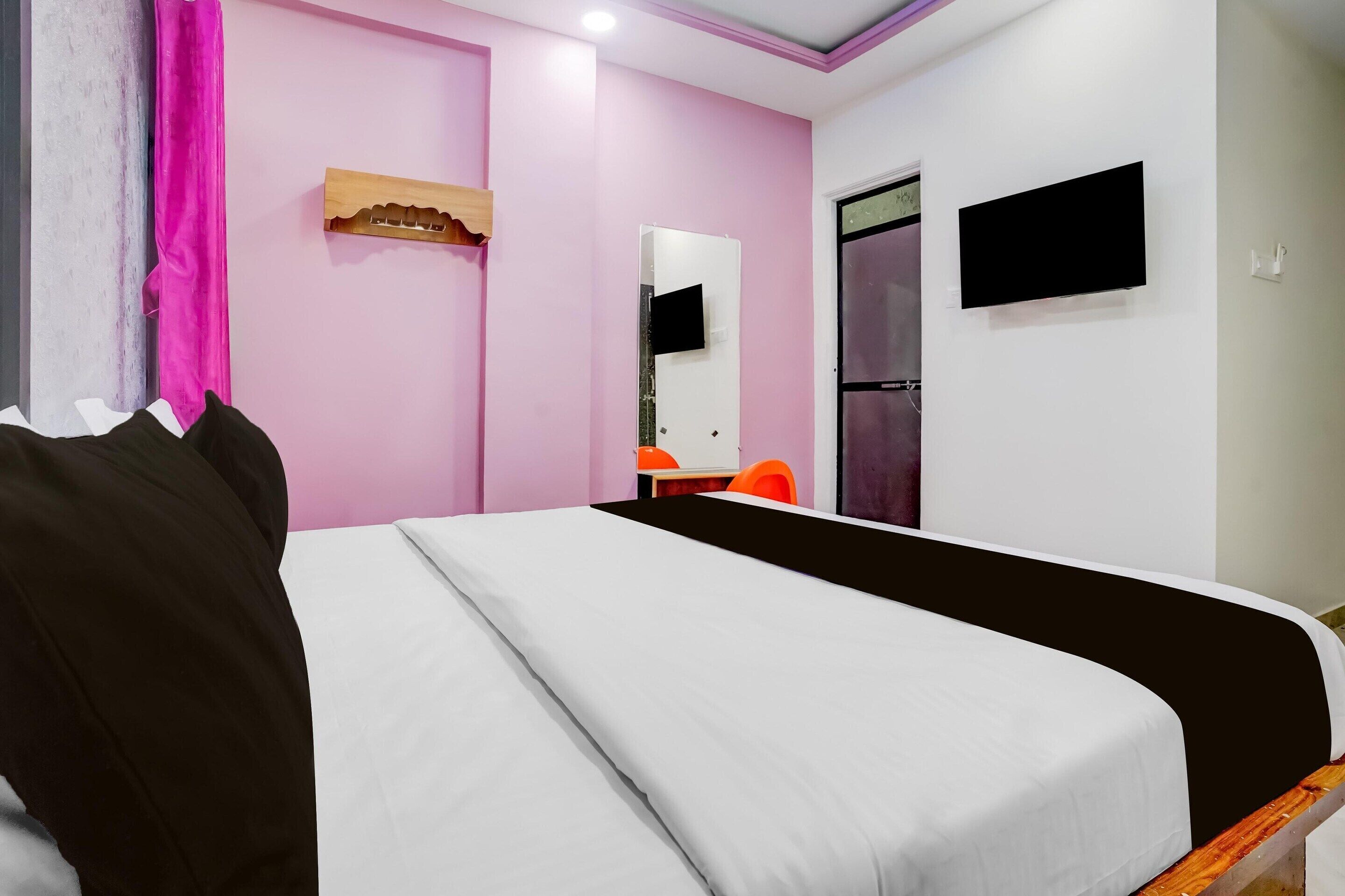 A hotel room with a bed, a TV, a mirror, and a door.
