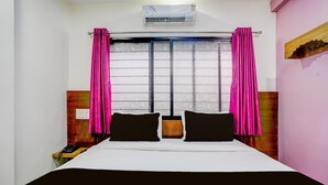 A hotel room with a bed, two pillows, a nightstand, a phone, and a window with curtains.