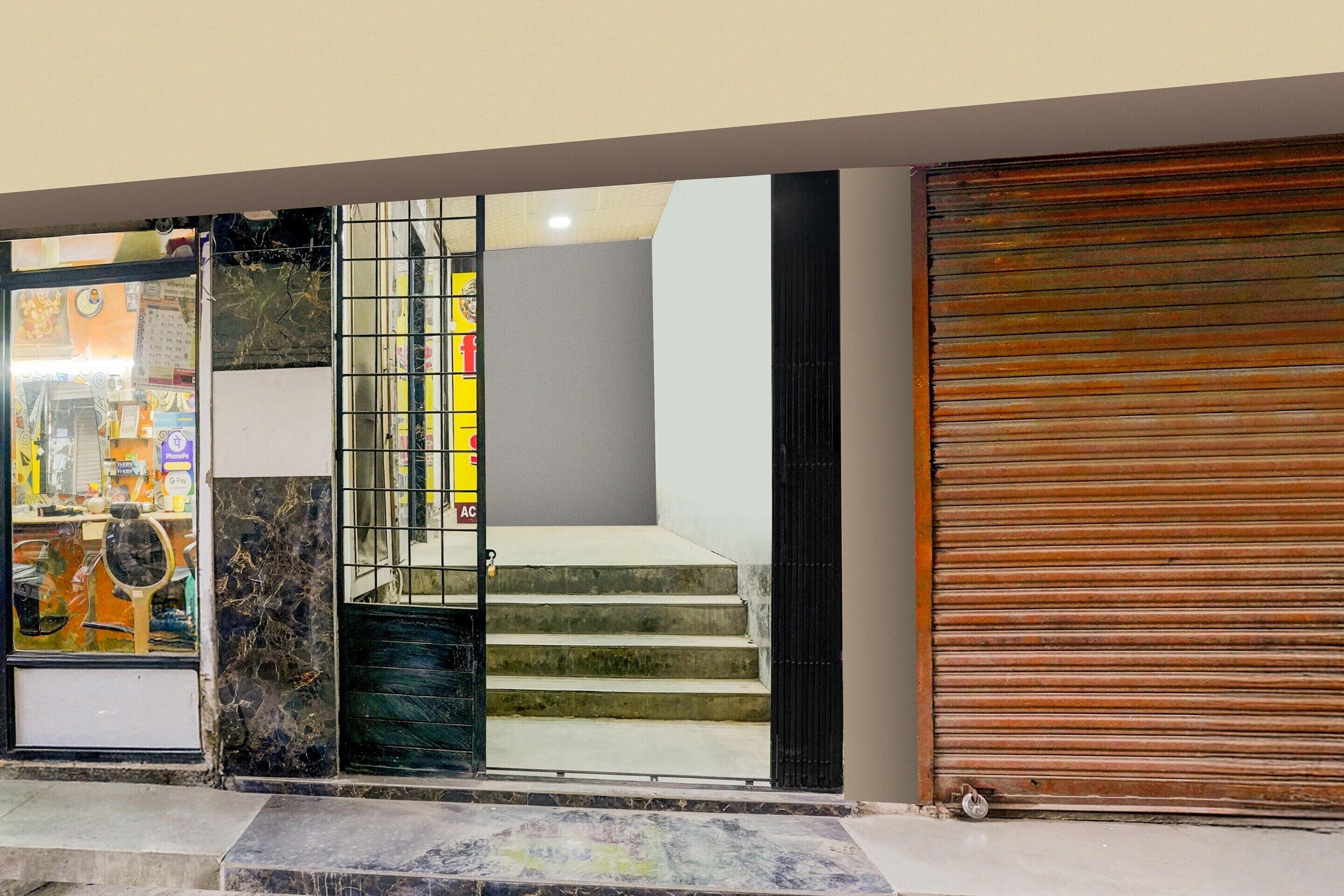 A building entrance with a closed metal gate, a set of stairs leading to a landing, and a closed wooden shutter door.