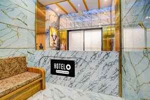 A hotel reception area with a marble wall, a sofa, and a sign indicating it's company-serviced.