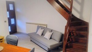 Una habitació amb una escala de fusta, un sofà, una taula de dinar amb cadires i un radiador.