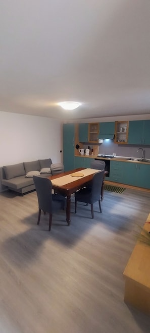 A living room with a sofa and a dining table with chairs. There is a kitchen area with cabinets and a sink.