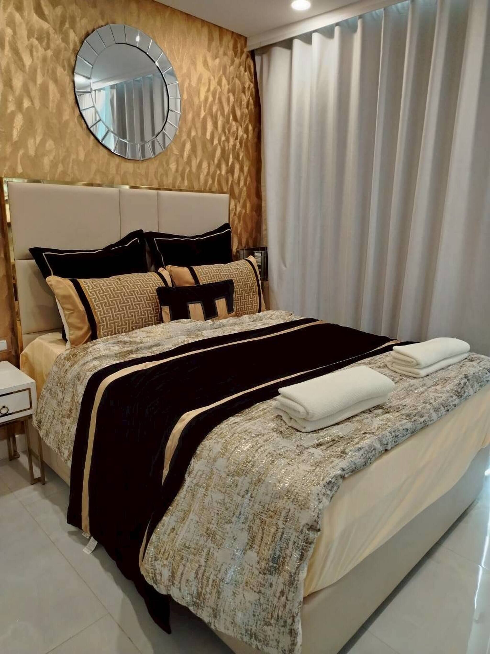 A neatly made bed with a headboard, a bedside table, and a wall-mounted mirror.