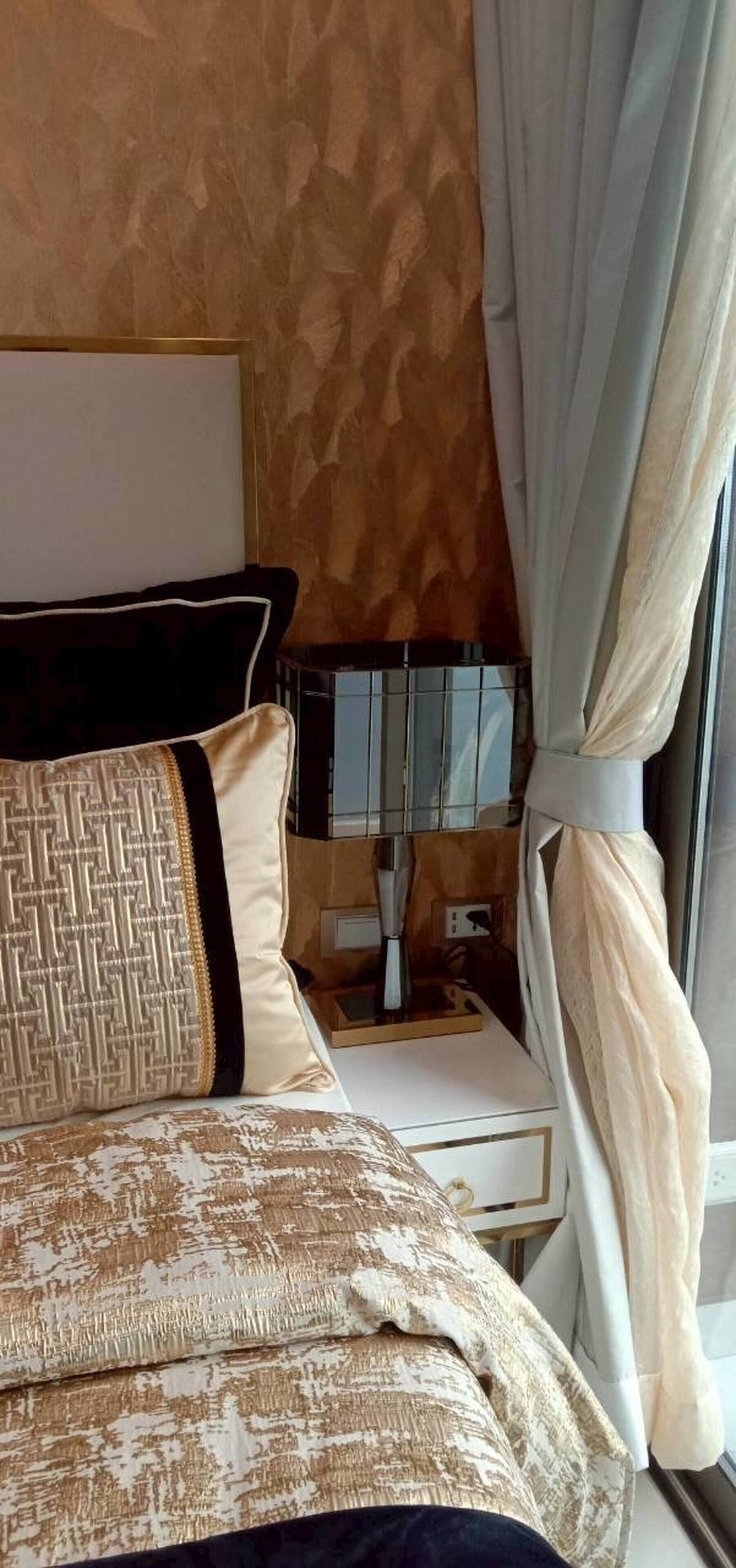 A bed with patterned bedding, a bedside table with a lamp, and a window with curtains.