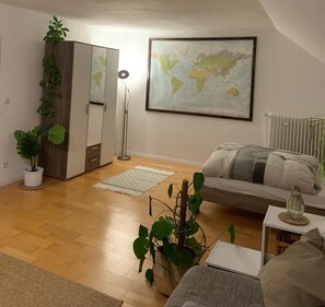 A living room with a sofa, a coffee table, a world map on the wall, a radiator, and potted plants. - Worker's Apartment in Lehrte near Hannover – up to 2 Guests (Lehrte)