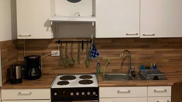 A kitchen with white cabinets, a stove, an oven, a clock, and wooden flooring.