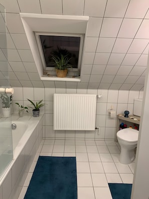Ein Badezimmer mit Badewanne, Toilette, einem Fenster mit Pflanze und einem Handtuchhalter.