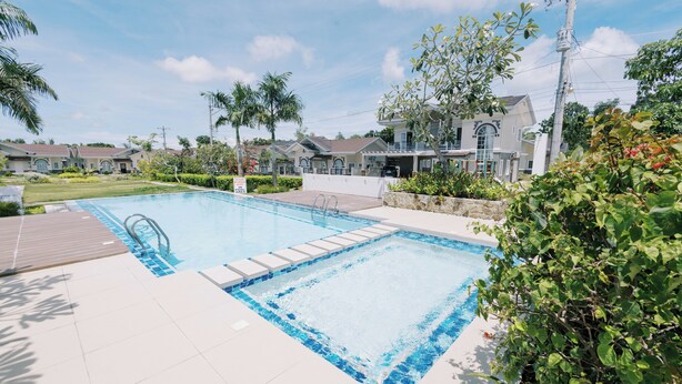A swimming pool with a wooden deck, surrounded by greenery and residential buildings. - 3BR Guesthouse near Panglao • Pool • Bohol Tours (Dauis)