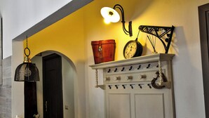 A room with a white door, a wall-mounted clock, a hanging light fixture, and a shelf with a decorative item. - Nivalu Apartment (Olbia)