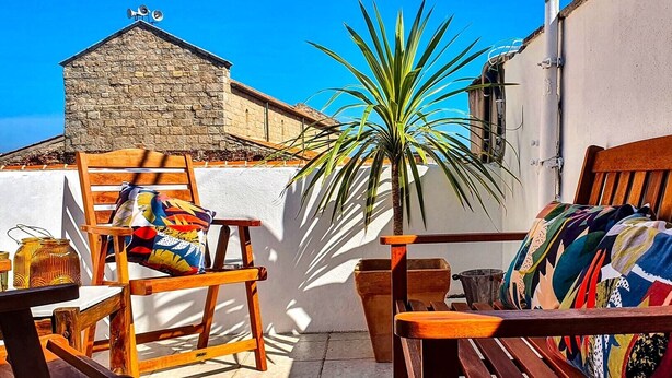 A wooden bench with colorful cushions, a stone building, and a palm plant in a sunny outdoor setting. - Nivalu Apartment (Olbia)