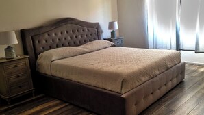 A bedroom with a large bed, two bedside tables, and a window with curtains. - Nivalu Apartment (Olbia)