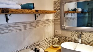 A bathroom with a wooden shelf holding towels, a hairdryer, and a mirror with a decorative frame. - Nivalu Apartment (Olbia)