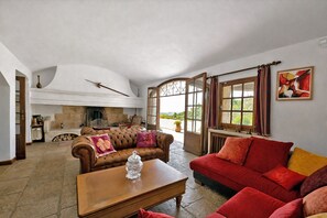 Un salón amplio con chimenea, un ventanal con cortinas y un sofá rojo.