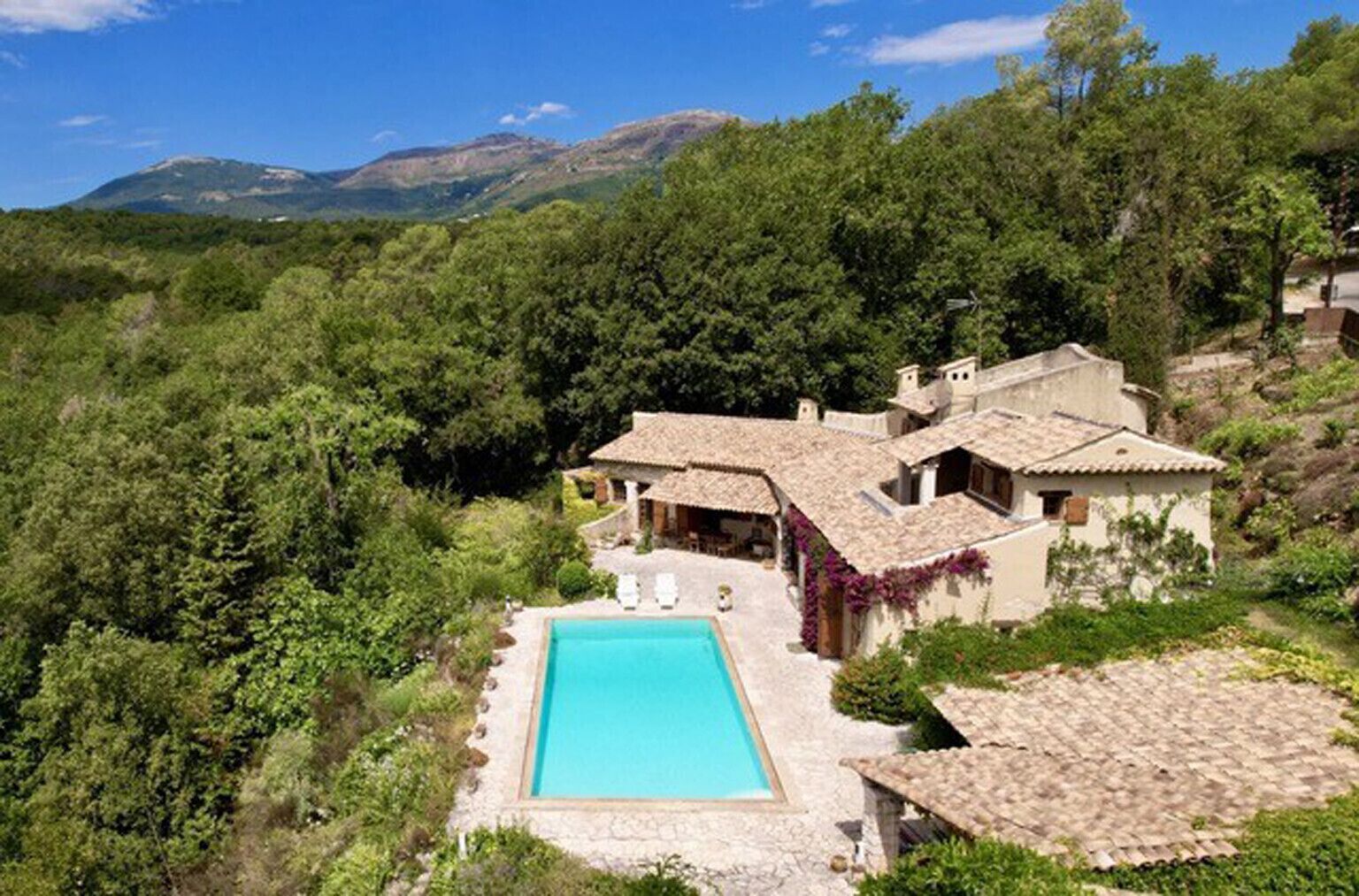 A villa with a swimming pool, surrounded by lush greenery and mountains in the background.
