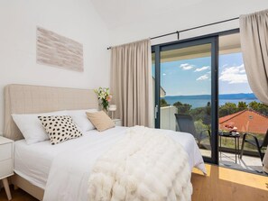 A bedroom with a bed, a nightstand, a vase with flowers, and a view of the sea through a glass door. - Sanctuary on the Rat Promenade (Bol)