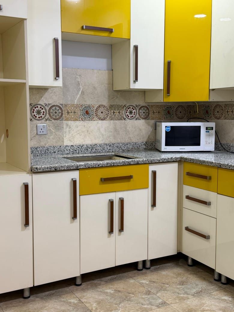 A kitchen with white and yellow cabinets, a microwave, and patterned tiles on the backsplash.