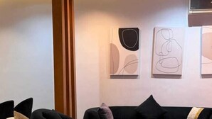 A modern living room with a black sofa, a white armchair, and a wooden coffee table. - ALSAWAH Warm 2BR - Casa Beverly Hills  (Sheikh Zayed City)