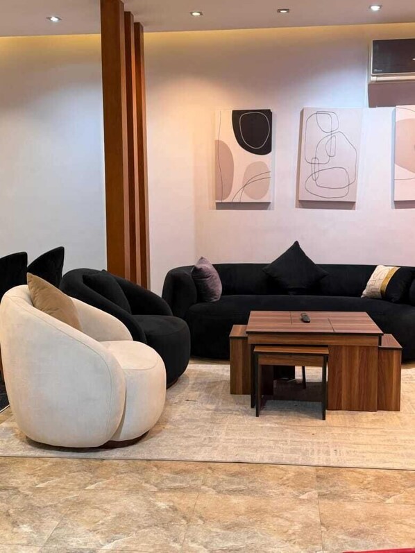 Uma sala de estar moderna com um sofá preto, uma poltrona branca e uma mesa de centro de madeira.