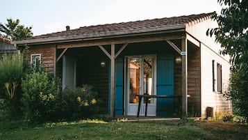 A wooden house with a porch, a door with blue shutters, and a number '60' sign on the wall.