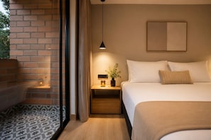 Une chambre d’hôtel moderne avec un mur en briques, un lit recouvert de draps blancs, une table de chevet avec une lampe et une œuvre d’art encadrée accrochée au mur.