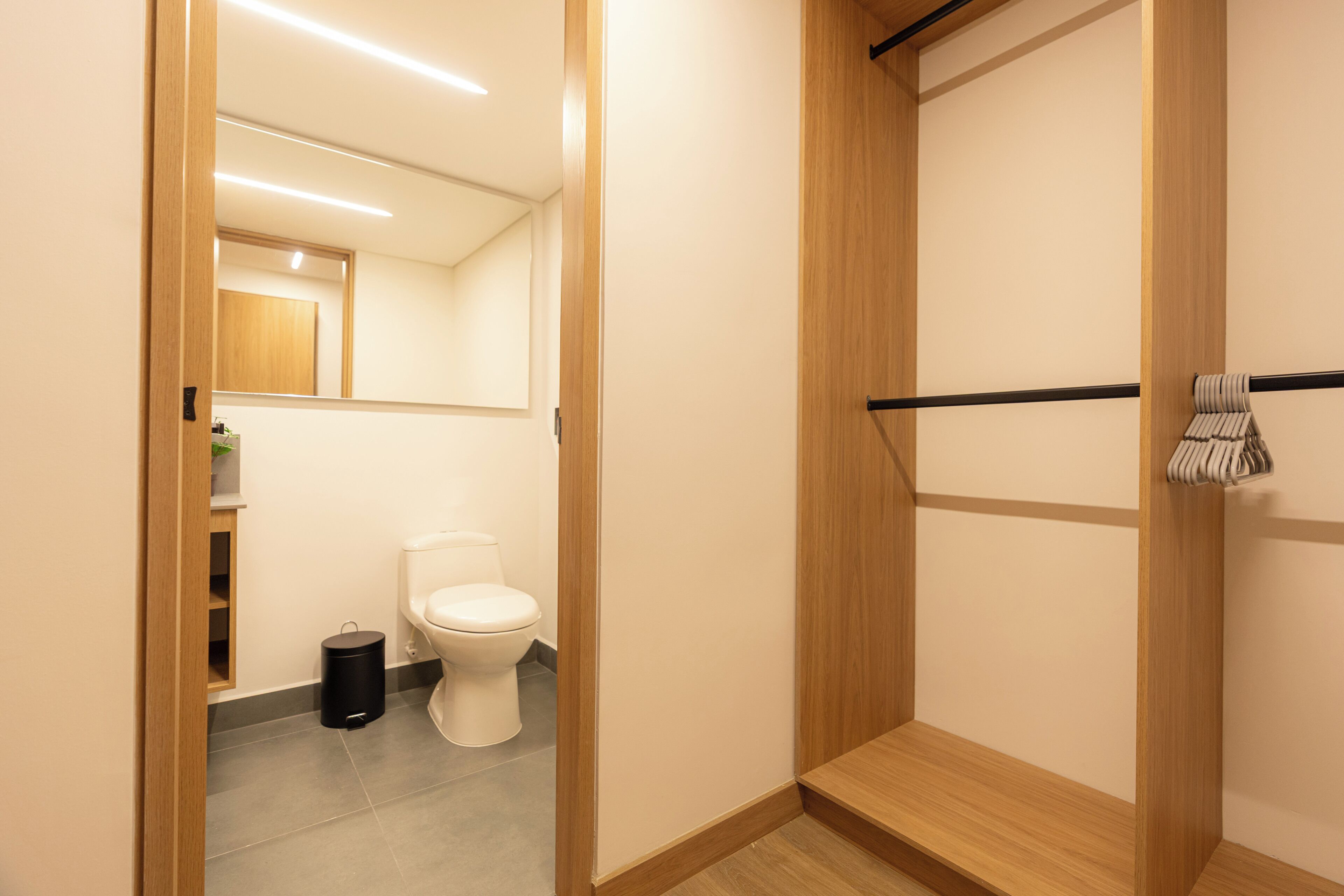 A modern bathroom with a toilet, a mirror, and a wooden shelf.