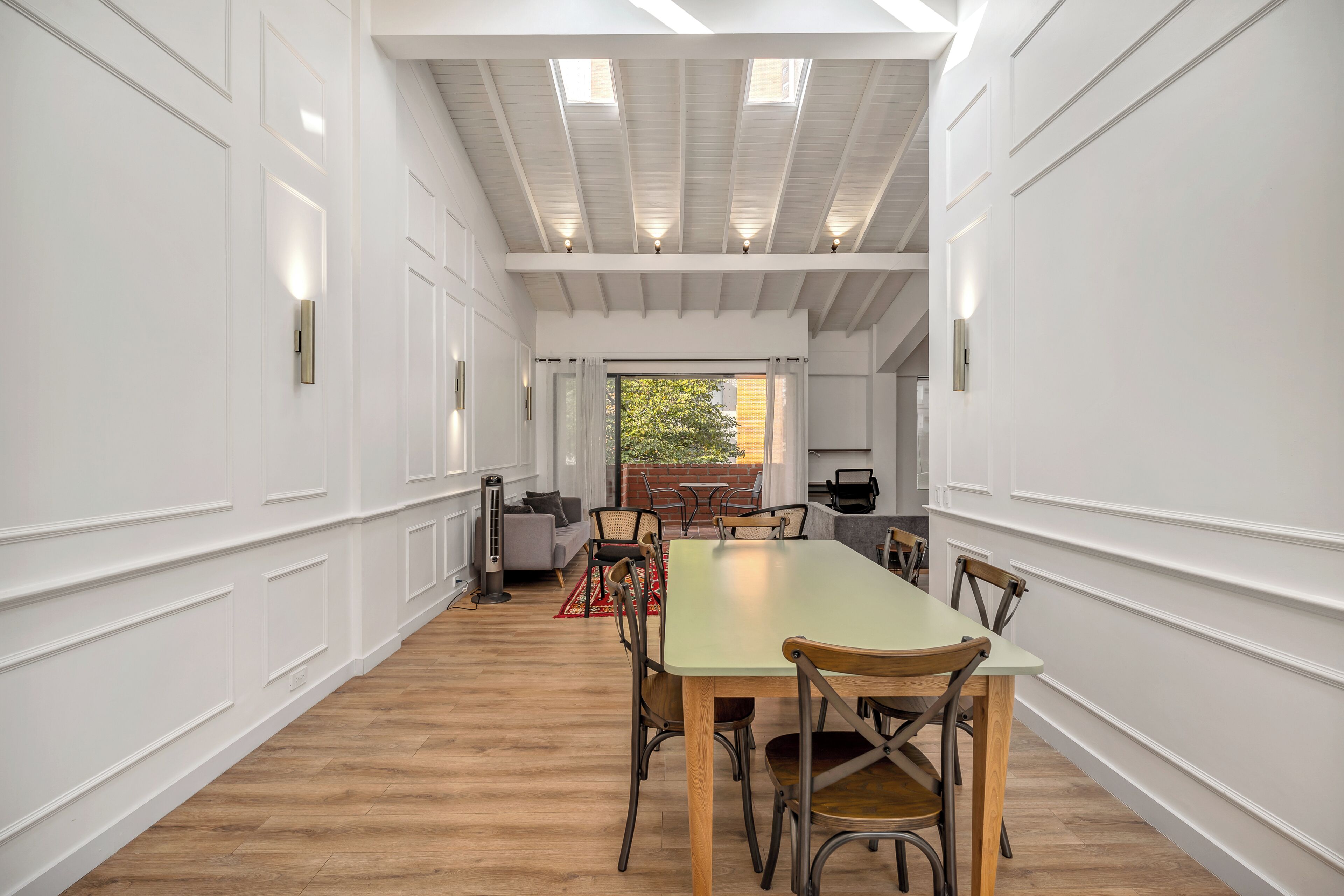 A long dining table with chairs, a sofa, and a radiator in a room with white walls and wooden flooring.
