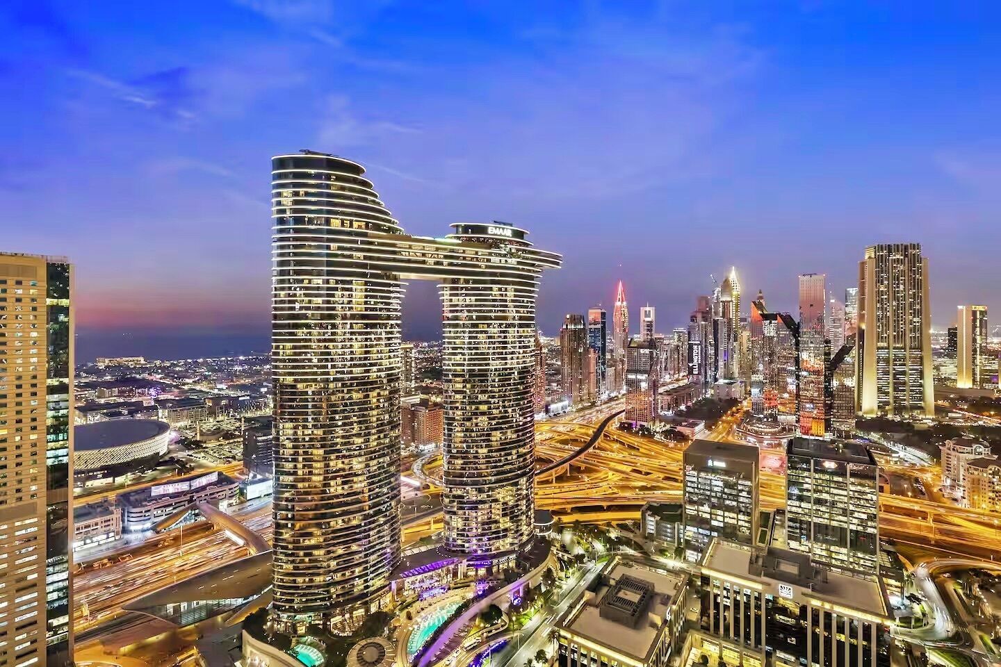A cityscape with modern high-rise buildings, including a distinctive curved structure and a tall building with a visible 'BMW' sign.