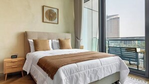 Et moderne hotelværelse med en stor seng, et natbord, et sengebord, et indrammet kunstværk og en balkon med udsigt over byen.