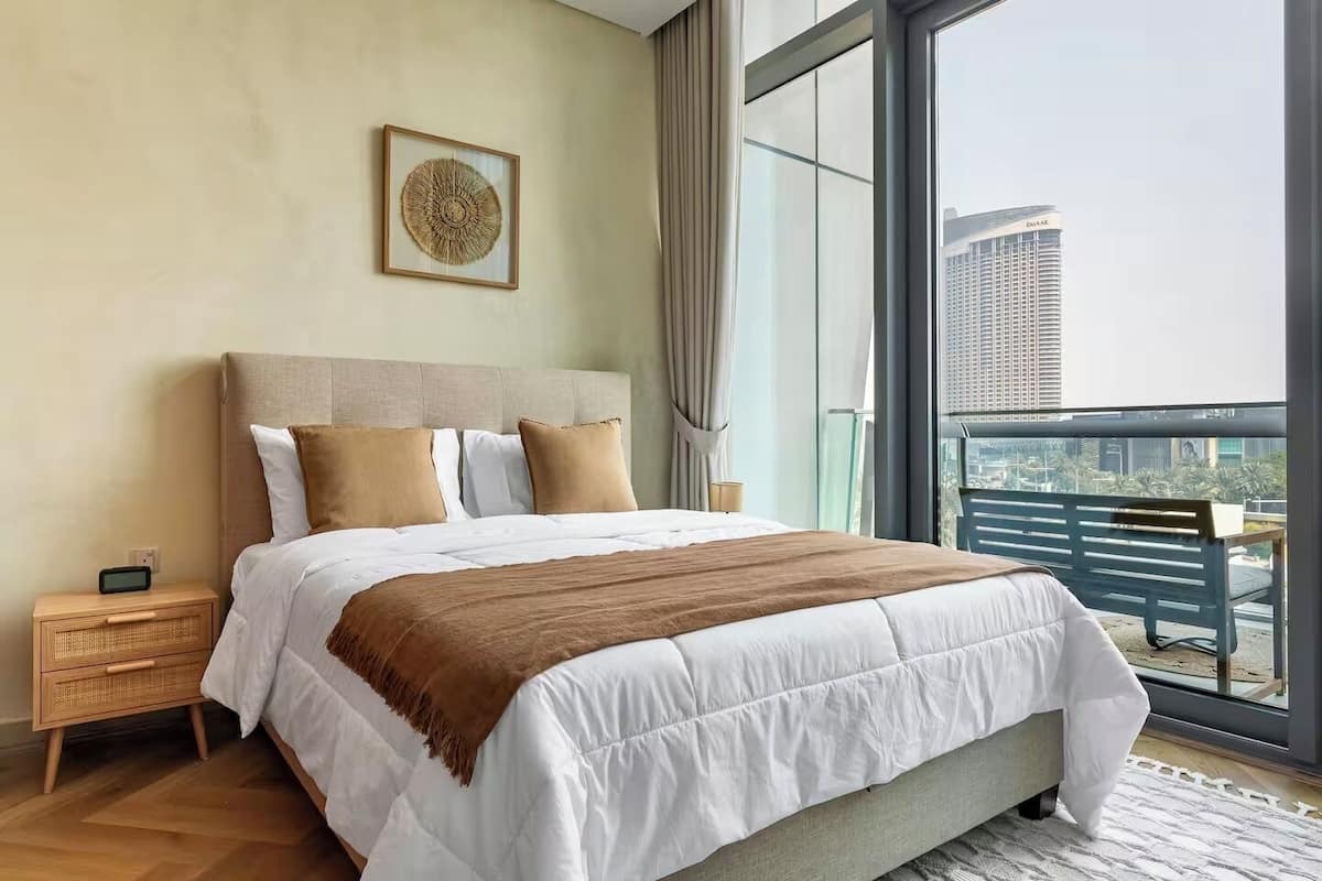 Una habitación de hotel moderna con una cama grande, una mesita de noche, una obra de arte enmarco y un balcón con vistas a la ciudad.