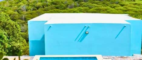Un espace piscine avec une structure bleue, un ciel dégagé et une colline verdoyante en arrière-plan.