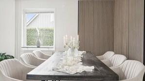 A dining area with a long table, six chairs, candles, and a vase with flowers.