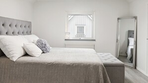 A bedroom with a large bed, a window, a radiator, and a mirror.