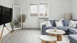 A modern living room with a grey sofa, two round coffee tables, a flat-screen TV on a stand, and a large window with a view of the outside.