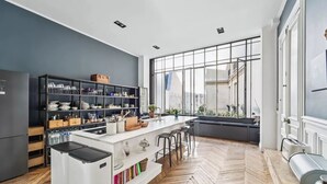 A modern kitchen with a central island, wooden herringbone flooring, and large windows offering a view of the city. - A 300m² Estate of Art, Elegance & Architectural Majesty:Blvd.de la Tour-Maubourg (Paris)