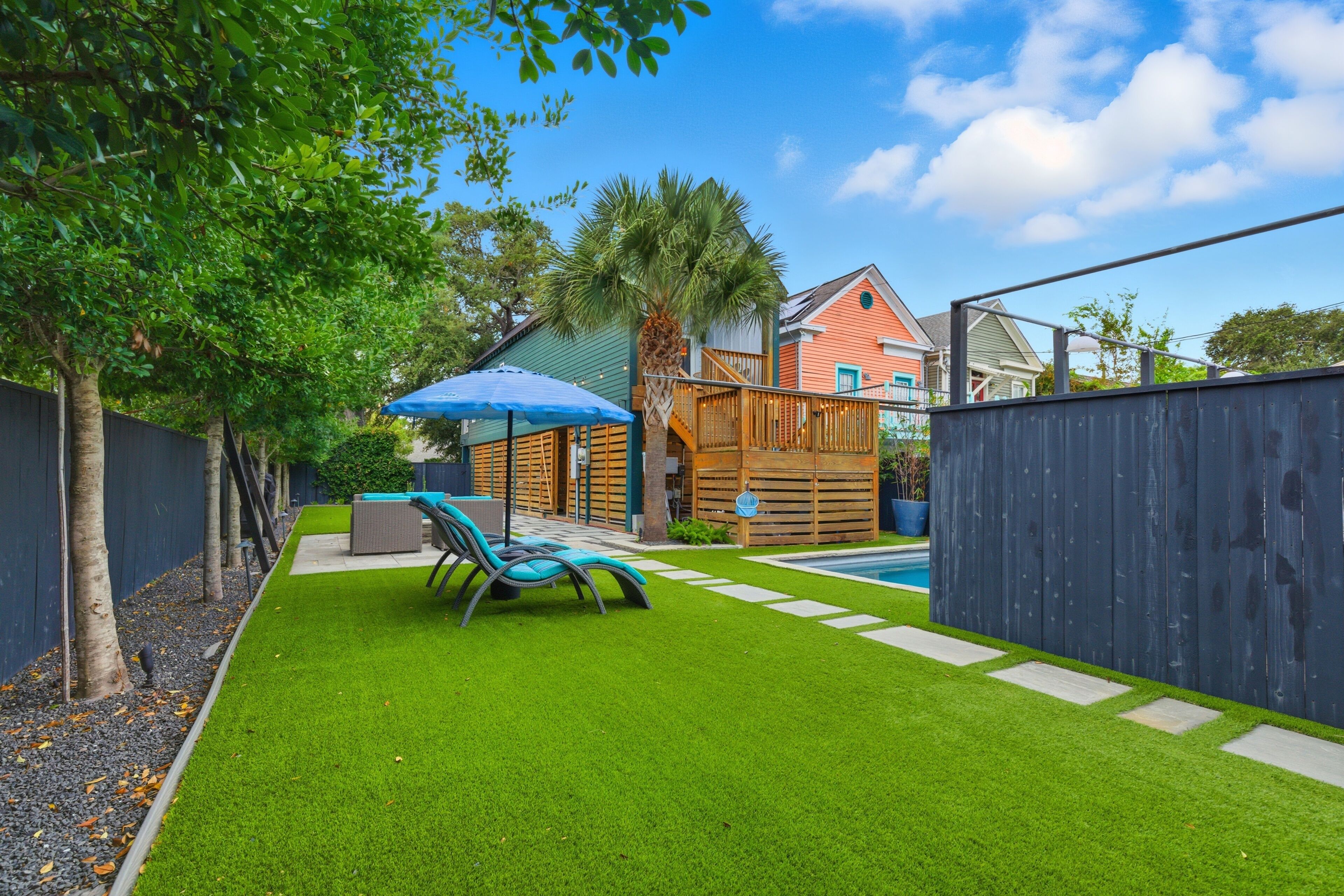 A backyard with artificial grass, a pool, a wooden deck, and a blue umbrella.