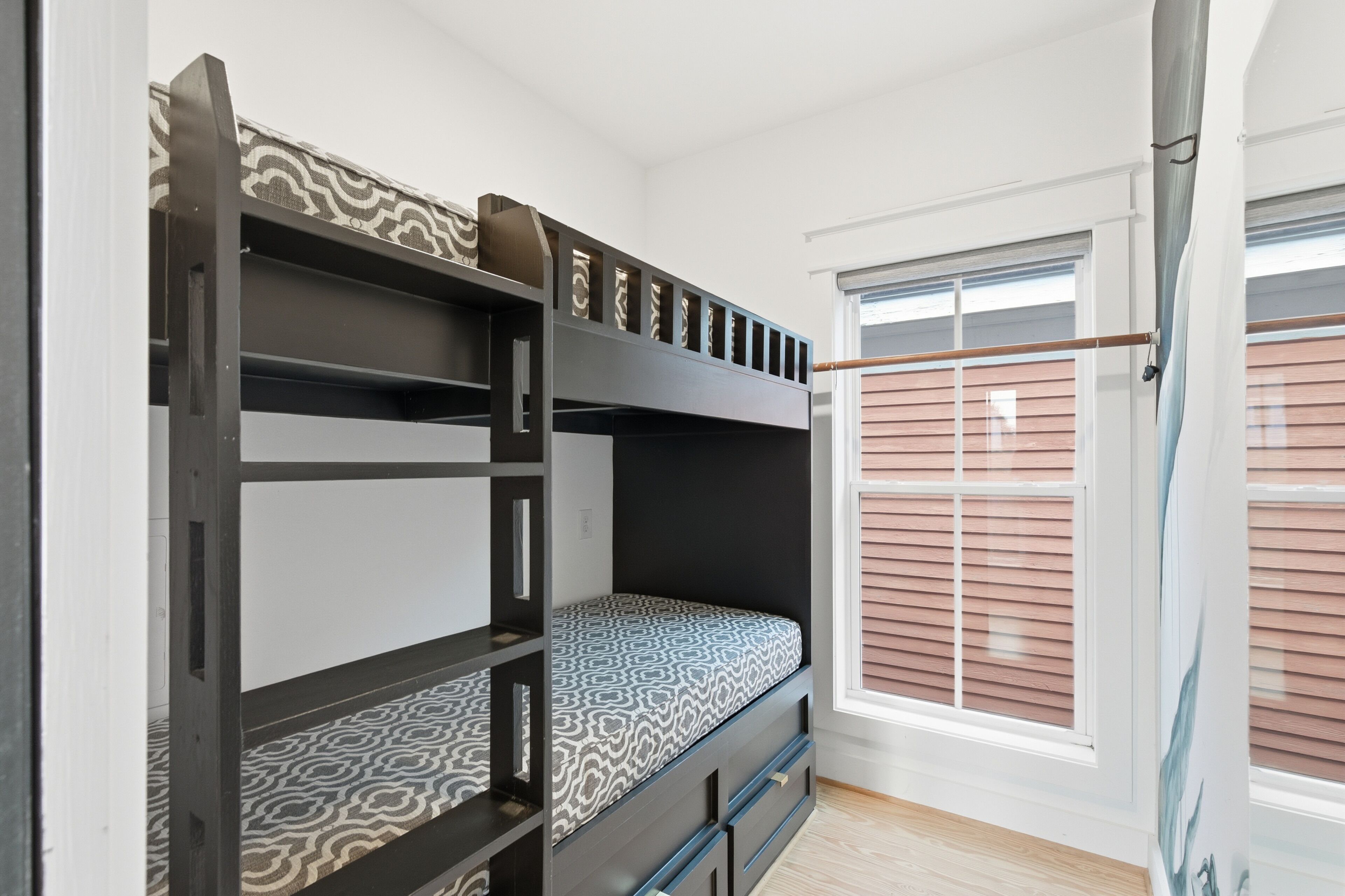 A bunk bed with patterned bedding, a window with blinds, and a door with a curtain.