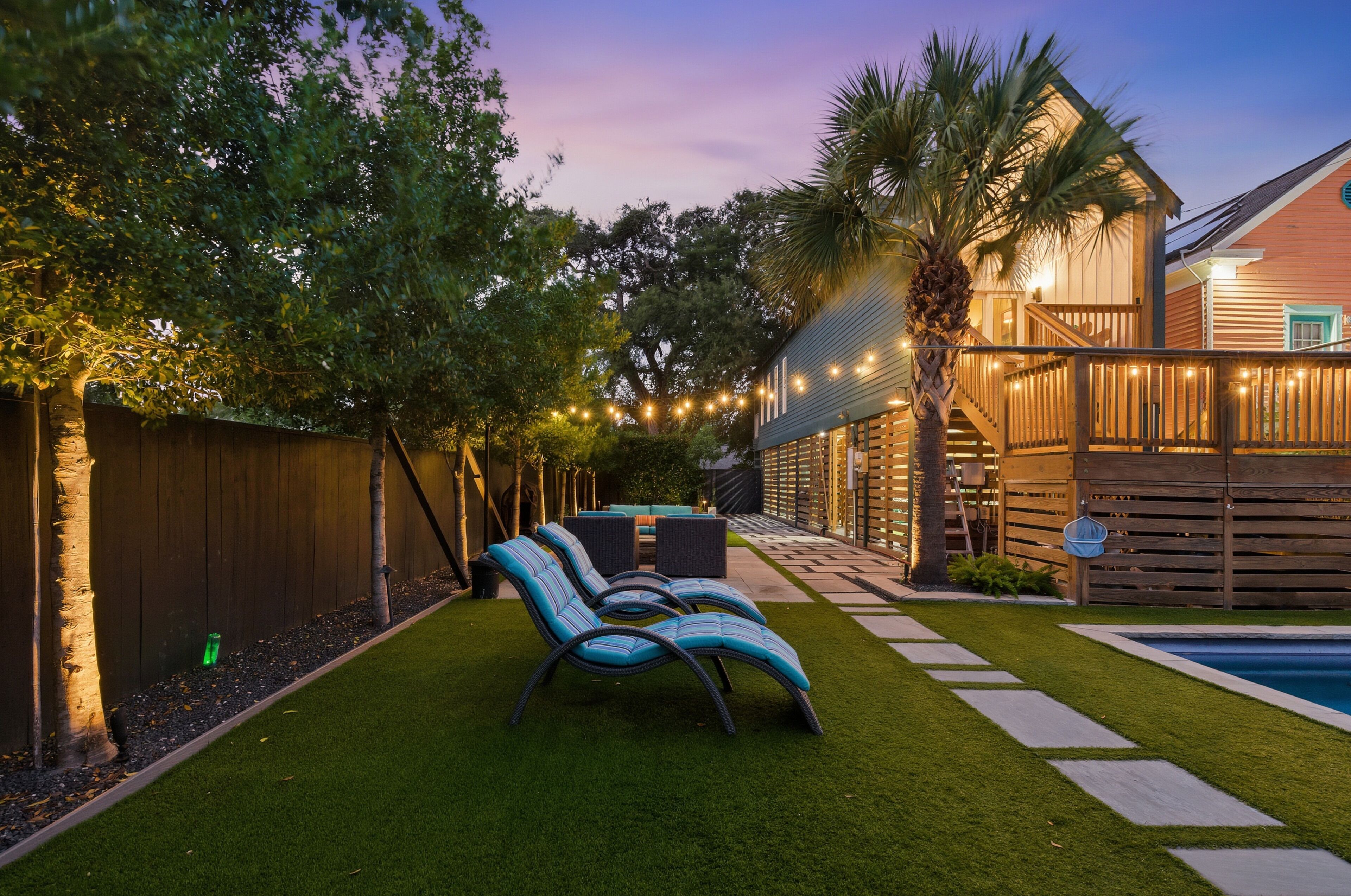 A backyard with a pool, artificial grass, and lounge chairs.