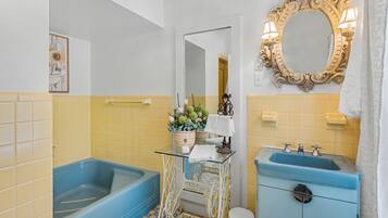 A bathroom with a blue bathtub, a white vanity with a blue sink, a mirror with a decorative frame, and a yellow-tiled wall.