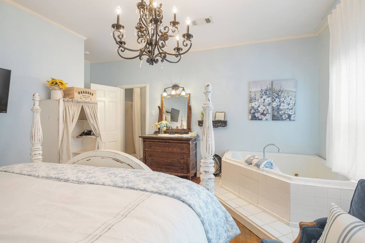 Un dormitorio con cama con dosel, tocador con espejo, bañera y candelabro.