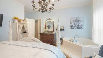 A bedroom with a four-poster bed, a vanity with a mirror, a bathtub, and a chandelier.