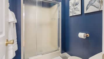 A bathroom with a glass shower door, a toilet, and two framed botanical prints on the wall.