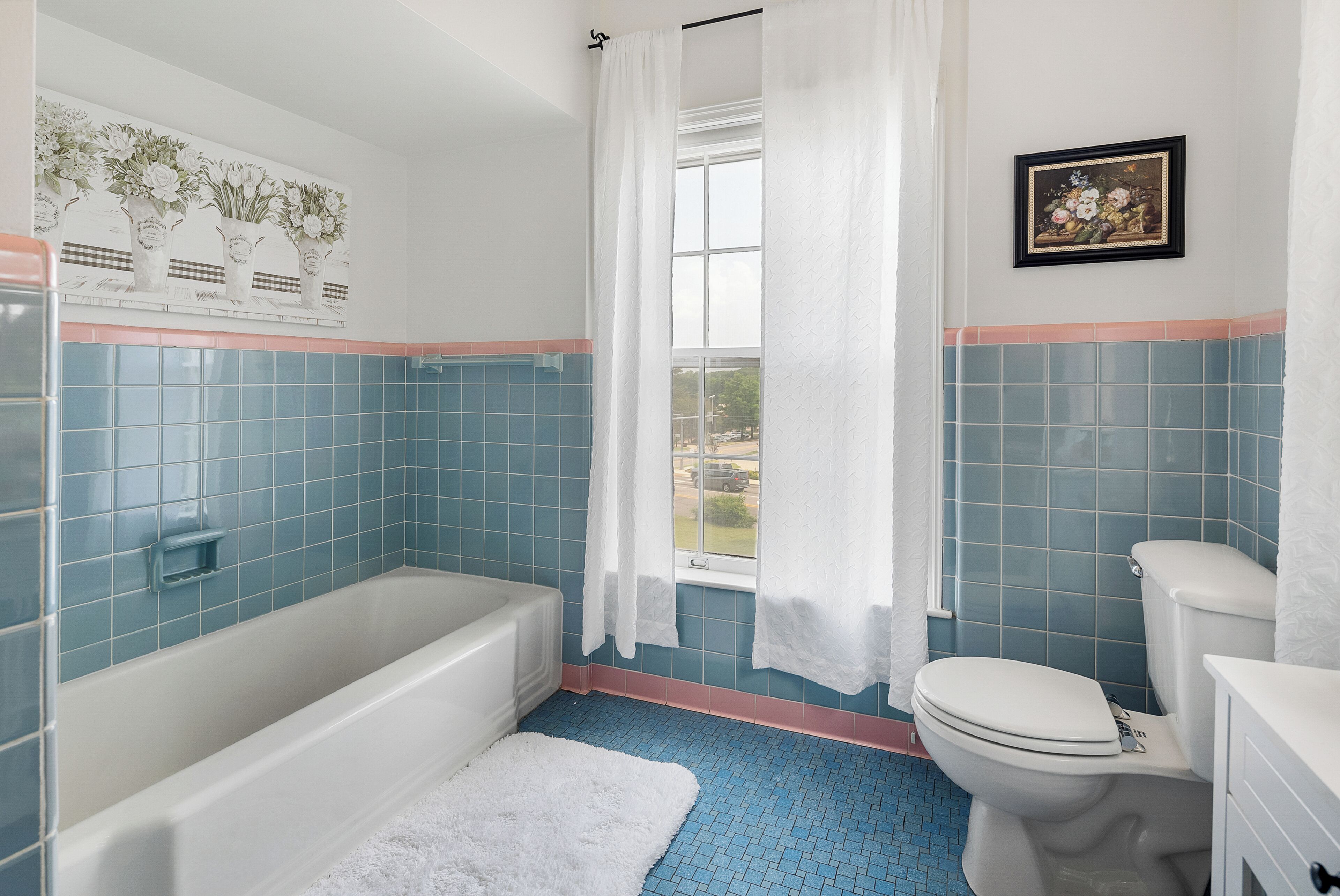 Une salle de bain avec une baignoire, des toilettes et une fenêtre avec des rideaux.