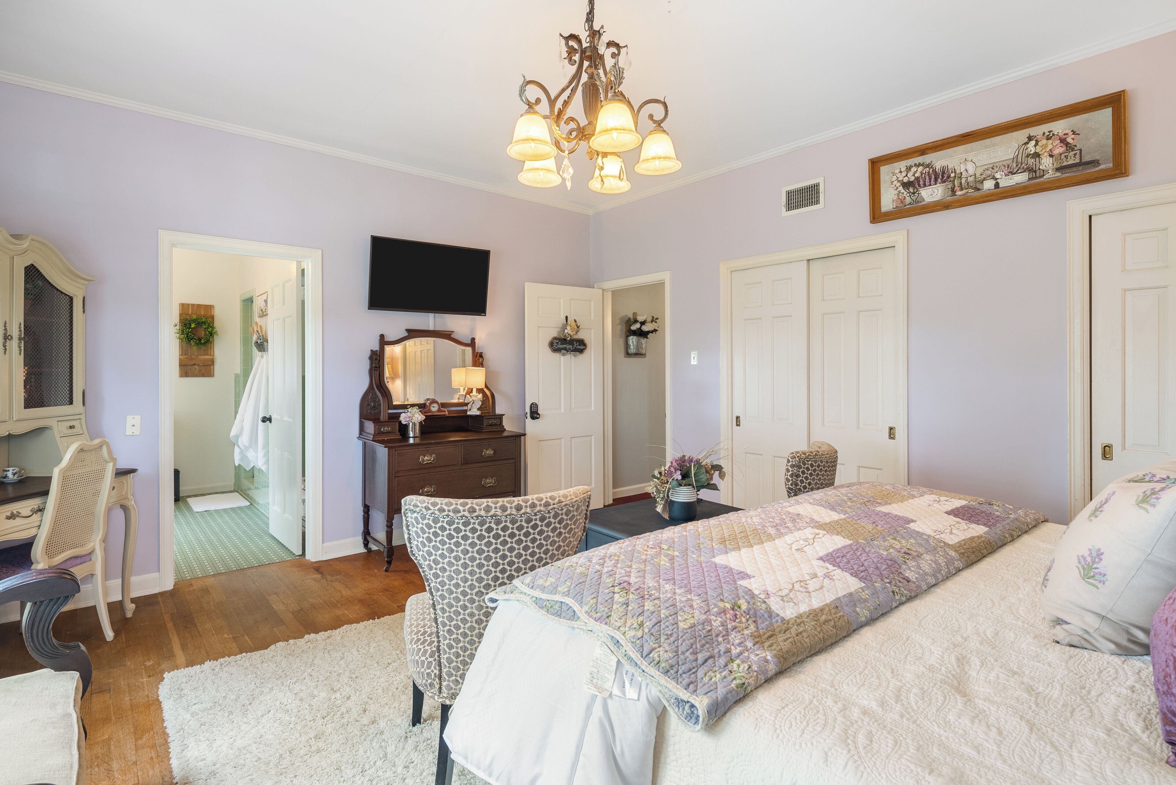Un dormitorio con cama, escritorio, silla, cómoda, espejo y candelabro.