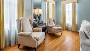 A room with two armchairs, a wooden floor, a large mirror, and curtains. - The Beland Mansion (Fort Smith)